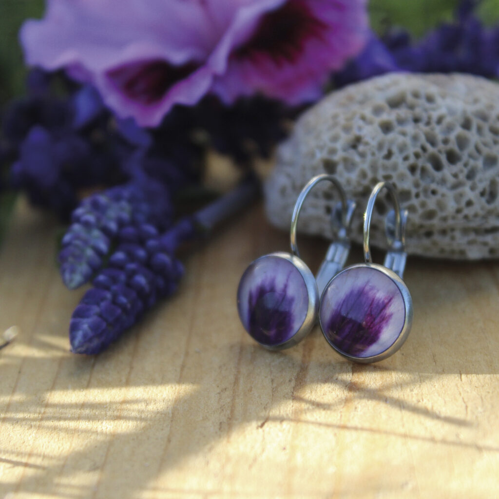 Pendientes redondos de acero hipoalergénico con pétalo de geranio natural encapsulado en resina, disponibles en cuatro tamaños, hechos a mano en Malas Herbas Artesanía, artesanos gallegos.