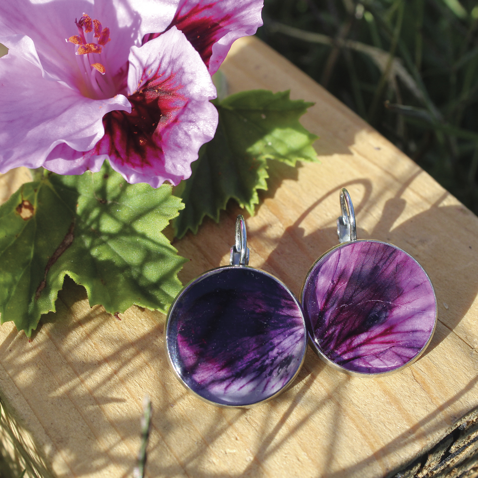 Pendientes redondos grandes (18 mm) de acero hipoalergénico con pétalo de geranio natural en resina, hechos a mano en Malas Herbas Artesanía, artesanos gallegos.