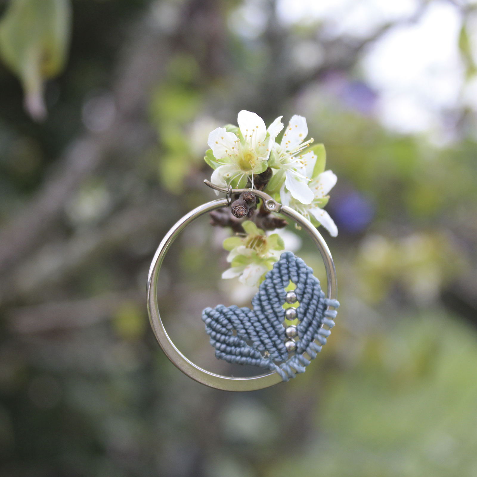 Pendientes de aro de acero plateado con hojitas de macramé en color azul, hechos a mano en Malas Herbas Artesanía, artesanos gallegos.