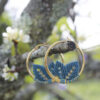 Pendientes de aro de acero dorado con hojitas de macramé en color azulón, hechos a mano en Malas Herbas Artesanía, artesanos gallegos.