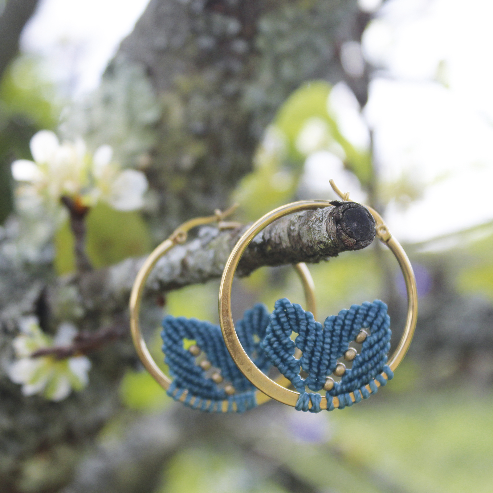 Pendientes de aro de acero dorado con hojitas de macramé en color azulón, hechos a mano en Malas Herbas Artesanía, artesanos gallegos.