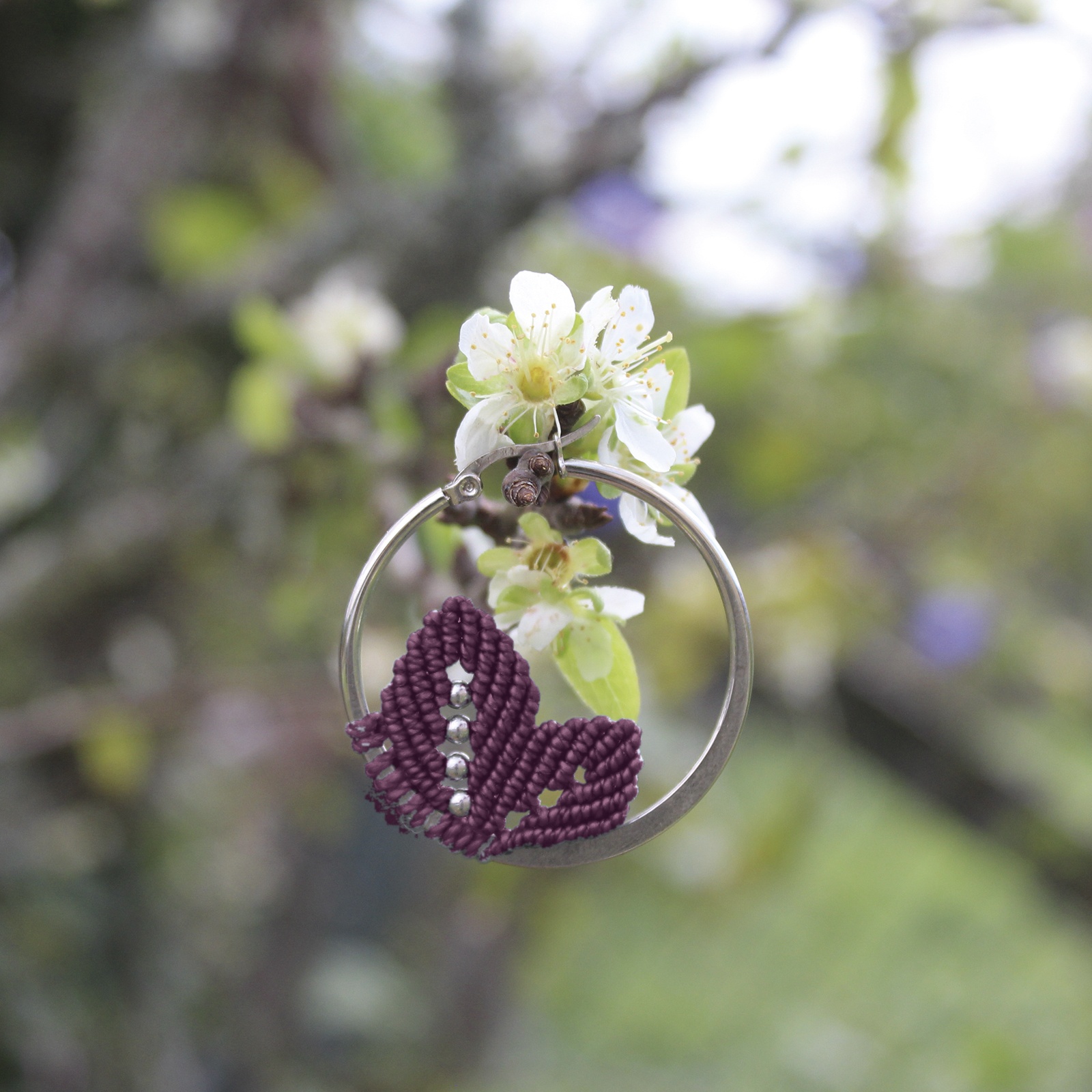 Pendientes de aro de acero plateado con hojitas de macramé en color ciruela, hechos a mano en Malas Herbas Artesanía, artesanos gallegos.