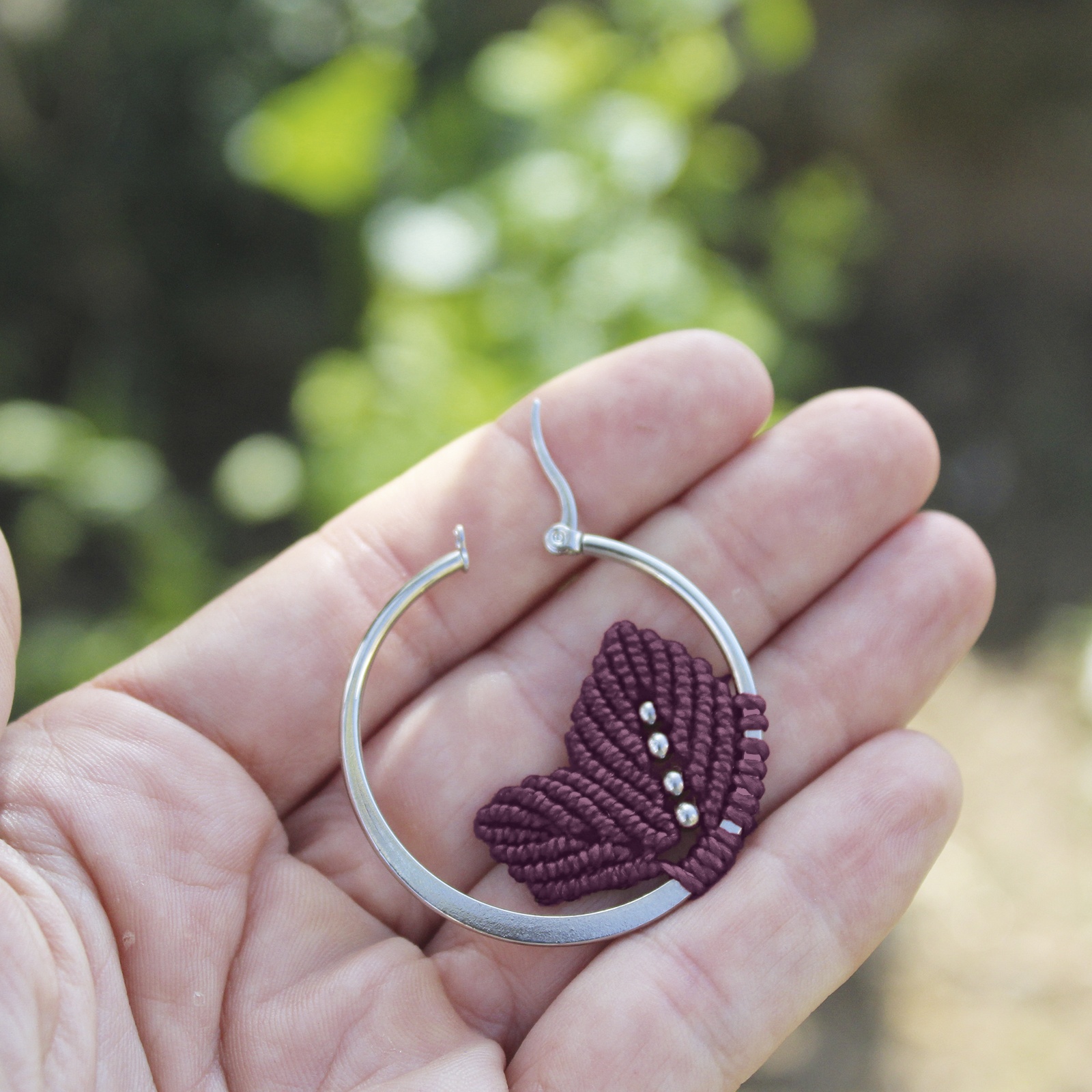Pendientes de aro de acero plateado con hojitas de macramé en color ciruela, hechos a mano en Malas Herbas Artesanía, artesanos gallegos.