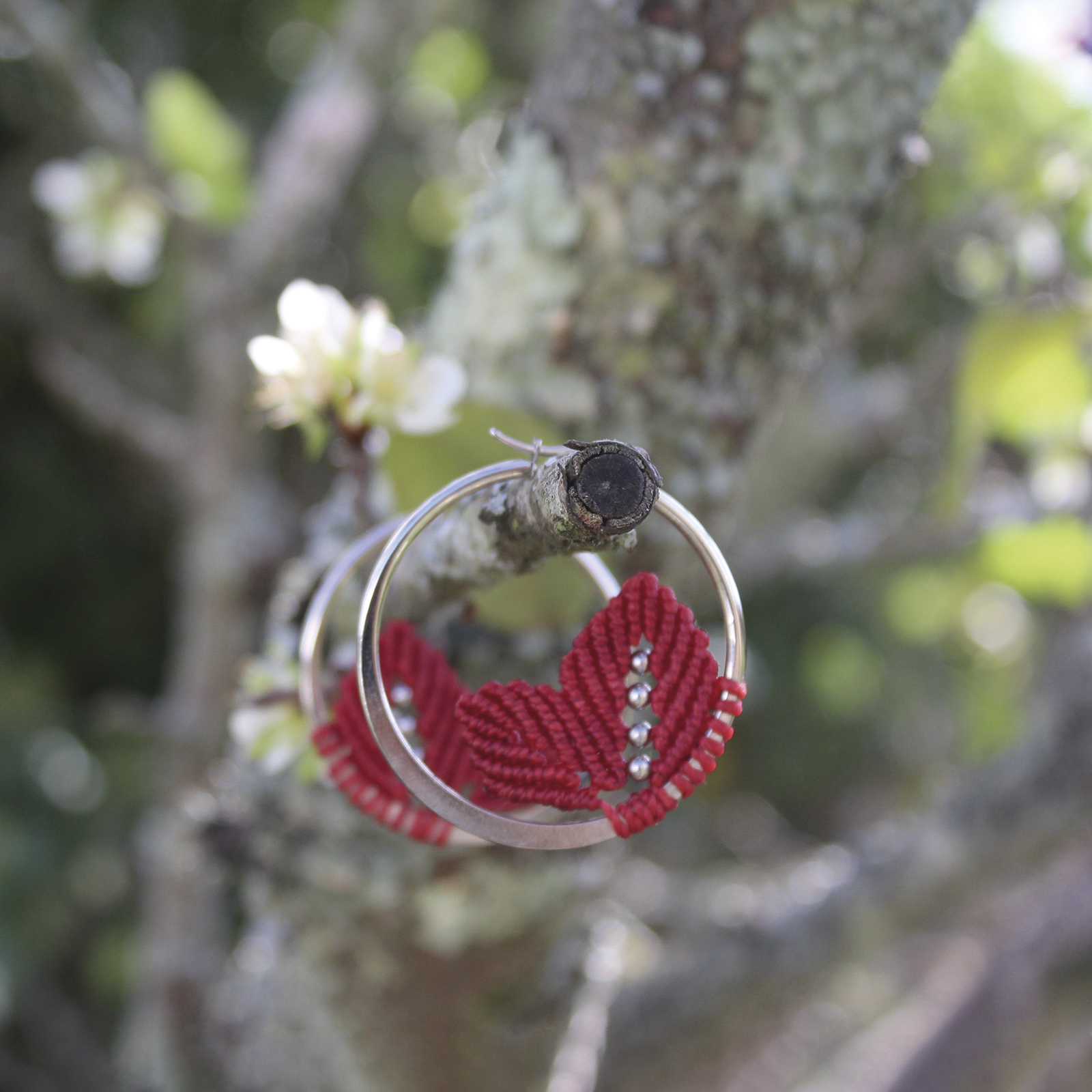 Pendientes de aro de acero plateado con hojitas de macramé en color rojo, hechos a mano en Malas Herbas Artesanía, artesanos gallegos.