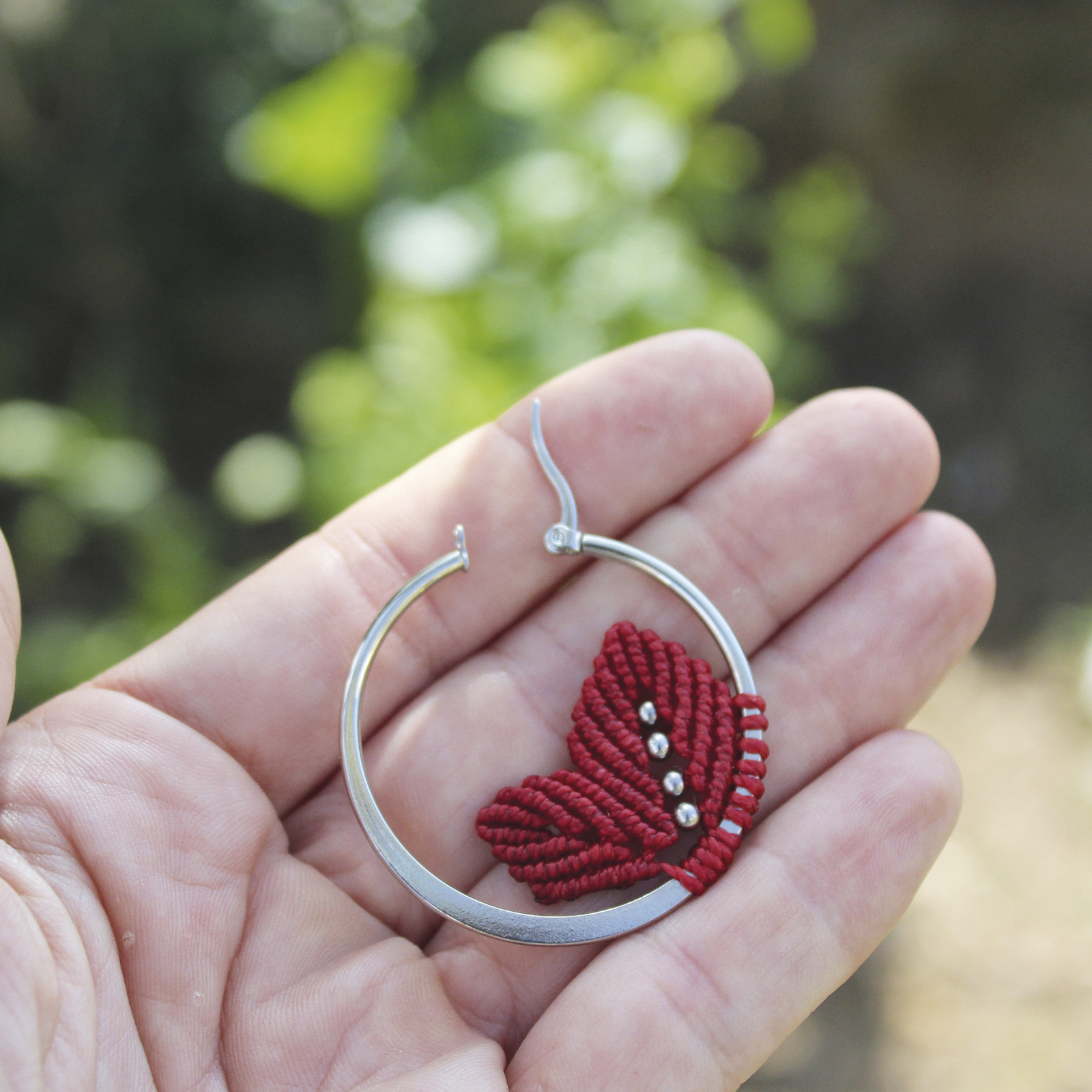 Pendientes de aro de acero plateado con hojitas de macramé en color rojo, hechos a mano en Malas Herbas Artesanía, artesanos gallegos.